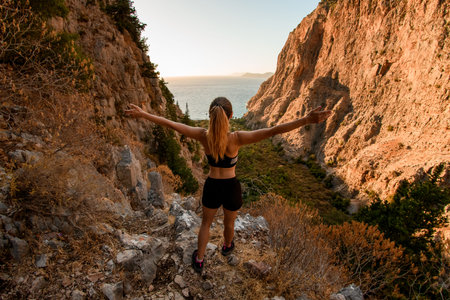 rear view of woman with arms to sides standing on stone and enjoying on view of landscape.