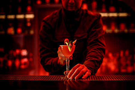 male bartender holds with his hand glass with alcoholic cocktail on bar counter.の写真素材