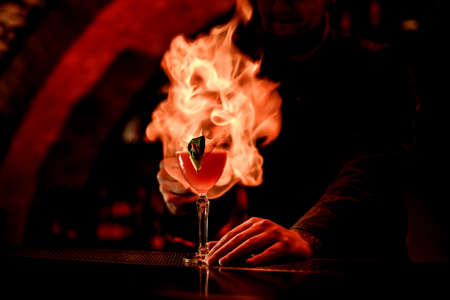beautiful view of glass with cocktail that bartender sets to fire at dark barの写真素材