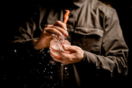 male bartender holds piece of ice and accurate crushes it with tridentの写真素材