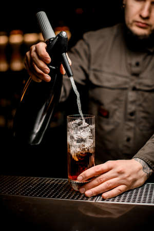 bartender adds carbonated liquid from siphon to transparent glass with cocktailの写真素材