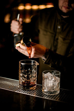 Male bartender pours drink from jigger into crystal mixing cup