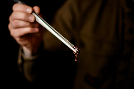 man s hand holds tweezers with beautiful small pine cone from which syrup flowsの写真素材