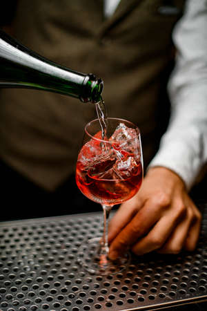 view of transparent glass full of ice cubes in which bartender pours drink from bottleの写真素材