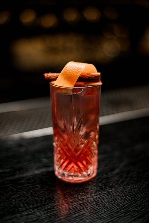 crystal glass with bright cold alcoholic cocktail decorated with zest and cinnamon.