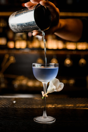 close-up of beautiful glass into which bartender pours blue cocktail from steel mixing cup