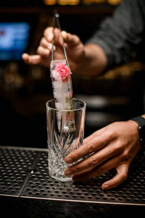 man at bar holds piece of ice with tongs and puts it into crystal glassの写真素材