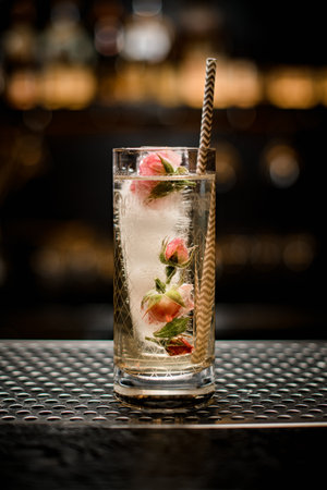front view on glass with drink and frozen rosebuds inside it and steel drinking tubeの写真素材