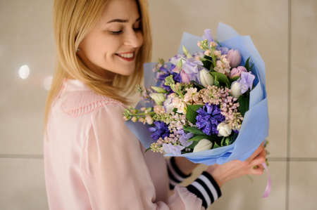 happy blonde woman holds floral bouquet of different fresh spring flowers in her handsの写真素材