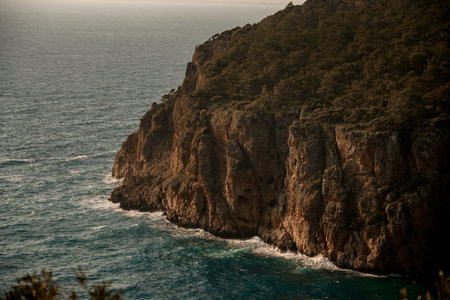Close-up view of large rocks with green trees near the water of sea coast. Beauty of natureの写真素材