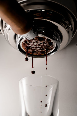 Drops of hot espresso coffee drink pouring through portafilter into clear glass
