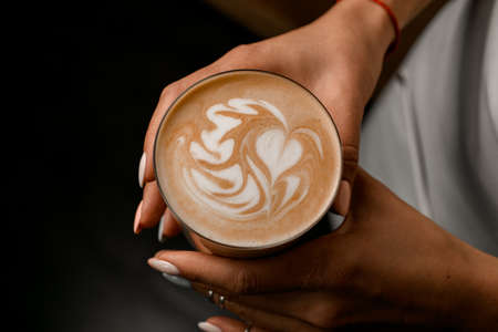 Great view of glass with coffee drink in hands of woman. Beautiful pattern on foamの写真素材