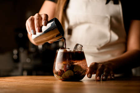 womans hand holds steel cup and carefully pours coffee into bowl with cold herbal drinkの写真素材
