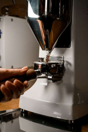 professional automatic coffee grinder pours ground coffee into portafilter in hands of baristaの写真素材