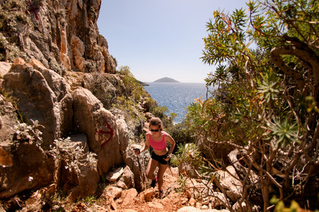 young woman with trekking poles in her hands climb up the rocky trailの写真素材