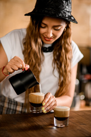 female barista accurate pours whipped milk cream in glass with coffee drinkの写真素材