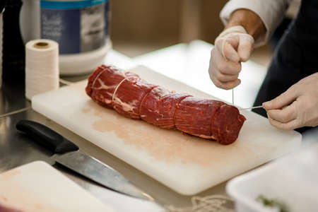 Close-up view of meat and male hands which tie it with butchers twineの写真素材