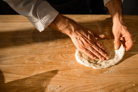 Close-up view of male chefs hands who adjusts the dough on on wooden table.の写真素材