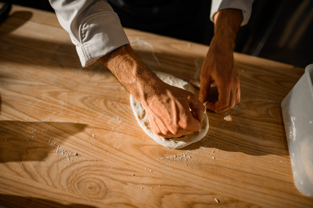 Close-up view of male chefs hands who neatly adjusts the dough on on wooden table