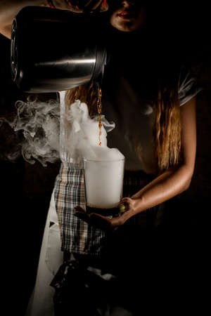 woman pours drink from coffee pot into transparent steaming glass in her handの写真素材