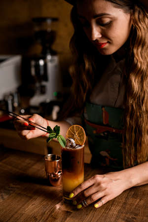young handsome woman neatly decorates glass with bumble coffee with mint leafの写真素材