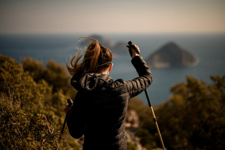 close-up rear view of woman with hiking poles against a blurred seascape background