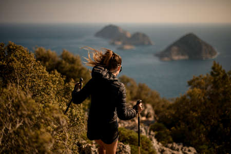 rear view of woman walking down the trail with hiking poles. Blurred seascape at backgroundの写真素材