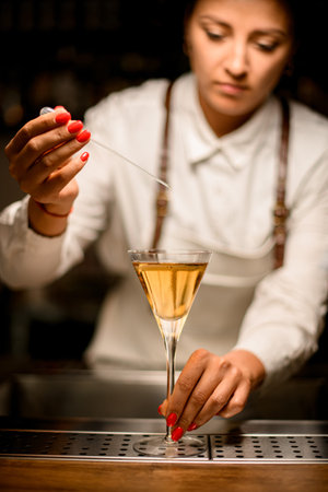 glass with drink stands on the bar and bartender adds essence using pipette