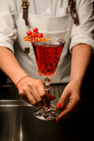 crystal glass with drink decorated with caramel and red currant in female handsの写真素材