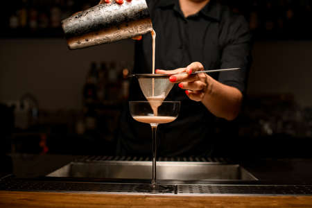 bartender pours drink into glass by filtering it through sieve.の写真素材