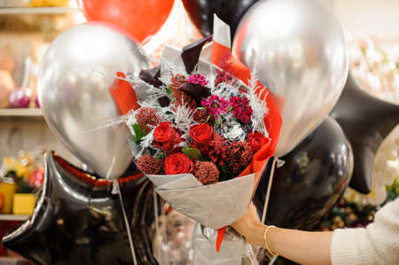 bouquet of roses and silvery and colored branches packed in wrapping paper in female handの写真素材