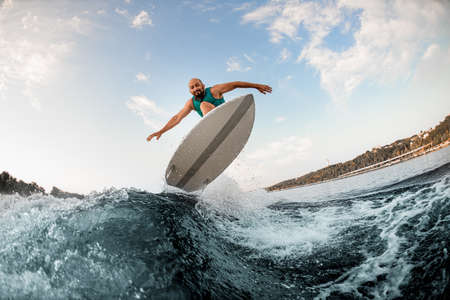 great view of man on wakeboard while skilfully jumping over splashing river wave against blue sky.の写真素材