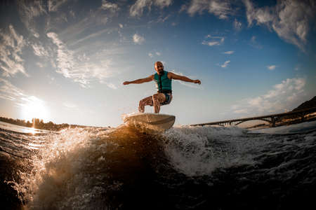 energetic sports man riding on wakeboard down the river waves against the blue sky and bridgeの写真素材