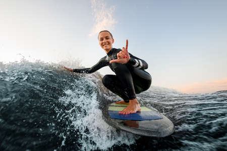 smiling woman sits on wakesurf board and rides the wave and touches the waves with one handの写真素材