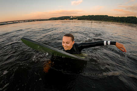 smiling woman in wetsuit swims in the water leaning on wakeboardの写真素材