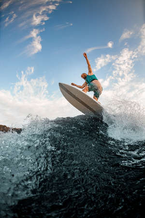 bottom view of man in a turquoise vest balancing on wakeboard on splashing wave of the riverの写真素材