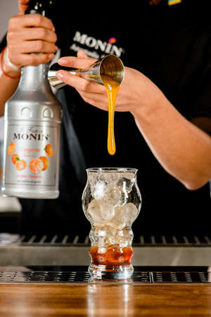 UKRAINE, KYIV - MARCH 11, 2021: view of clear glass of ice into which bartender pours orange syrup from steel jiggerのeditorial素材