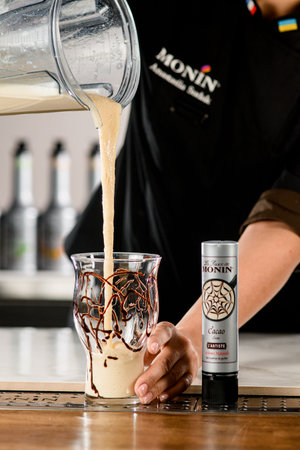 UKRAINE, KYIV - MARCH 11, 2021: Bartender pours whipped cocktail from blender bowl into glass