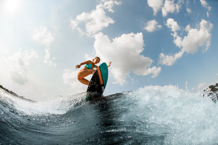 Energy woman having fun wakesurfing on the board on the river wave against blue sky