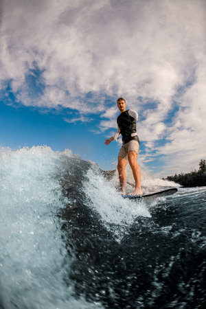 one-armed man ride the wave on wakeboard against the background of cloudy sky.の写真素材