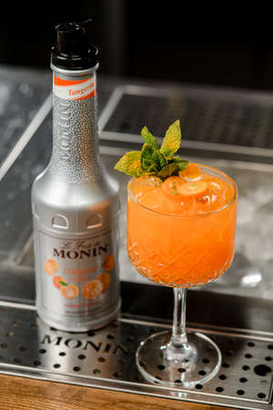 UKRAINE, KYIV - MARCH 12, 2021: top view of bottle of Monin Tangerine syrup and glass of bright orange cocktail on bar counterのeditorial素材