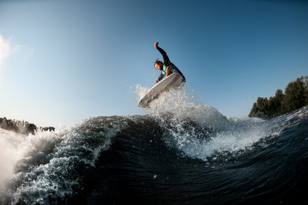 wakesurfer actively jumping on high wave on the background of blue sky