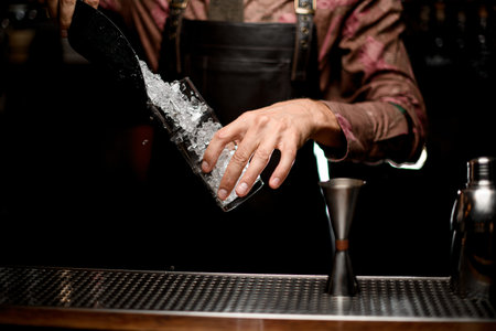 hand of man bartender holds glass and pours pieces of crushed ice from a scoop
