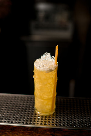 glass full of ice and bright yellow cocktail with drinking straws on the barの写真素材