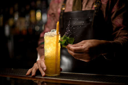 wonderful view of glass full of ice and cocktail with drinking straws and male hand with wet mint leavesの写真素材