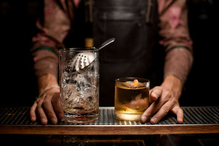 glassy mixing cup with ice and strainer on bar counter and glass with cocktail.の写真素材