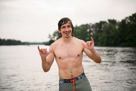 Cheerful young man shows gestures with his hands on the background of the riverの写真素材