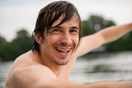 portrait of cheerful man with wet brown hair and braces on his teethの写真素材