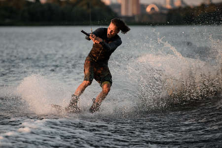 Athletic guy holds rope and speedly riding wakeboard on the river.の写真素材
