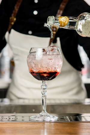 UKRAINE, KYIV - MARCH 12, 2021: Close-up view of crystal glass with ice and syrup and hand of woman bartender pours liquid from bottle into itのeditorial素材